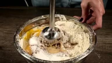 厨房里的一个糕点女孩在一个金属碗里用搅拌机打着面团做海绵蛋糕、面粉、鸡蛋和