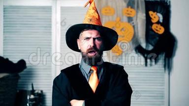 穿着女巫西装的留胡子`男人露出了鬼脸。 一个戴着橙色帽子的长胡子男人在万圣节的节日里做鬼脸