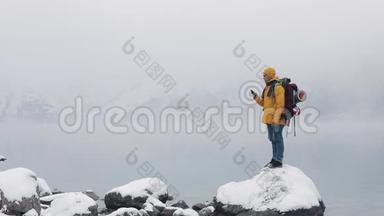 快乐旅行者在徒步冬<strong>季</strong>旅行中使用智能<strong>手机</strong>。 美国徒步旅行者站在山湖附近的石头上。 白雪公主