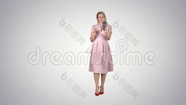 微笑的女人穿着粉红色的裙子，在<strong>渐变</strong>的背景下做<strong>视频</strong>呼叫和行走。