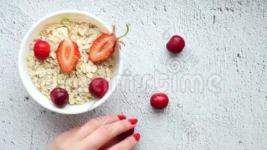 一张厨房桌子的细节<strong>照片</strong>，上面有一杯白色的燕麦片和<strong>草莓</strong>，还有一只手把<strong>草莓</strong>放在上面