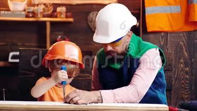 父亲，带胡须的家长教小儿子使用工具螺丝刀.. 孩子，忙着戴防护头盔的孩子