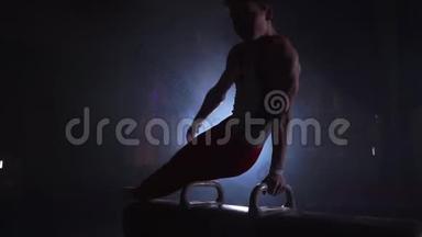 男子体操运动员在黑暗背景下，在鞍马上做倒立和旋转动作，并在慢动作中吸烟