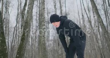 一个年轻人在冬天的森林里晨跑，累了，停下来喘口气。 他恢复了体力