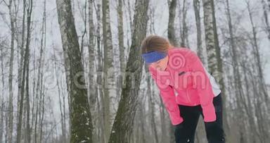 一个年轻的女人在冬天的森林里晨跑，累了，停下来休息，继续跑。 他恢复了<strong>体力</strong>