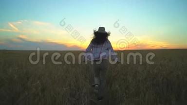夏季日落时，妇女游客在麦田里奔跑。 徒步旅行者女人戴着帽子，背着背包徒步旅行。 女孩
