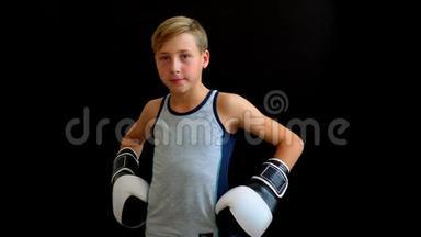 一个年轻的运动员站在黑暗的背景上。 男孩穿着灰色T恤，双手戴手套.. 黑白的