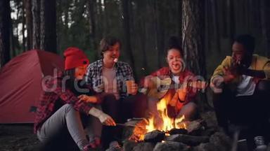快乐的冒险徒步旅行者围坐在炉火旁，唱歌弹吉他，吃棉花糖，拍手