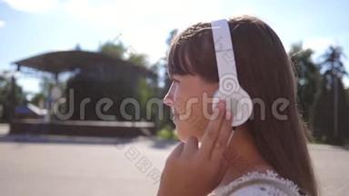 女孩带着耳机沿着城市<strong>街道</strong>行走，听<strong>音</strong>乐和微笑。 穿着白色长裙子的女孩
