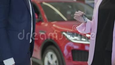 未识别的推销员给未识别的女商人一把汽车钥匙，并在汽车经销商中握手。 女孩颤抖