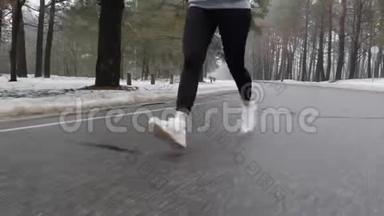 年轻迷人的白种人女孩在冬天带着耳机在雪地公园跑步。 特写双腿前方跟进射击
