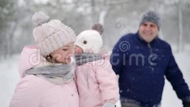 友好的全家人在降雪的情况下在冬天的森林里散步。 父亲、母亲和女儿