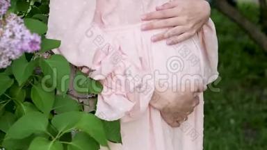 穿粉色连衣裙的孕妇特写腹部.. 一位穿着<strong>漂亮衣服</strong>的孕妇在公园里散步。 怀孕了
