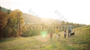 一个年轻家庭的后景，有两个小孩子和一只狗在秋天的大自然散步。