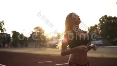 漂亮的长发黑发女郎穿着黑色比基尼在体育场慢跑。 整理和休息。 太阳照耀着