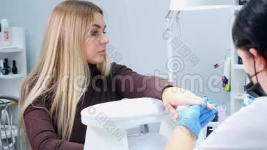 美甲医生正在一家美容院给客户的指甲涂上凝胶抛光剂。 竖起钉子。 刀片女孩失修指甲