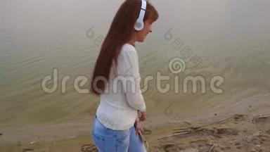 戴着耳机的女孩带着平板电脑去海滩听音乐，美丽的女孩笑着笑着