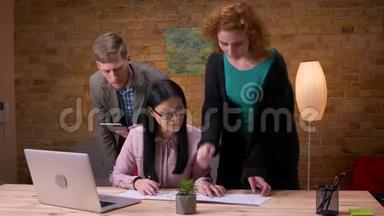 三名员工在办公室内使用笔记本电脑平板电脑和图表讨论数据的特写镜头