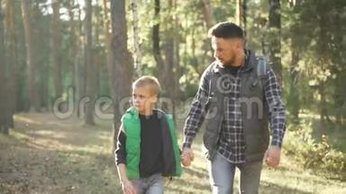 一个年轻的家庭留着胡子的男人和他可爱的儿子在火堆里徒步旅行，牵着手说话。 父爱