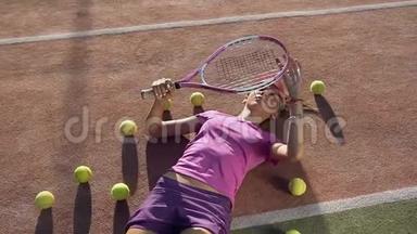 年轻女子躺在网球场上，拿着很多球，玩着网球拍。