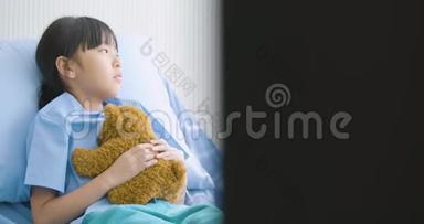 一个亚洲小女孩独自躺在医院里拥抱玩具，不幸的孩子失去父母，生病和治疗