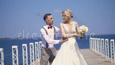 美丽的新婚夫妇，新娘和新郎在户外跳舞，在一个美丽的码头上，对抗蔚蓝的大海和天空。 夏季