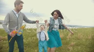 爸爸妈妈牵着孩子`手，举起他，一个年轻的家庭在田野上散步，阴天