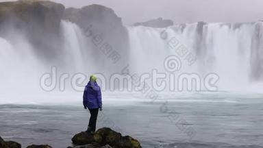 一个年轻的女人欣赏一个强大的狂暴瀑布，沿着岩石边缘重<strong>重地</strong>落下。 一条晶莹清澈的冰川水流