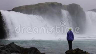 一个年轻的女人欣赏一个强大的狂暴瀑布，沿着岩石边缘<strong>重重地</strong>落下。 一条晶莹清澈的冰川水流