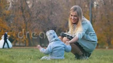 年轻的<strong>妈妈</strong>带着一个婴儿在秋天的公园里散步。 <strong>宝宝</strong>躺在草地上，<strong>妈妈</strong>帮他起床