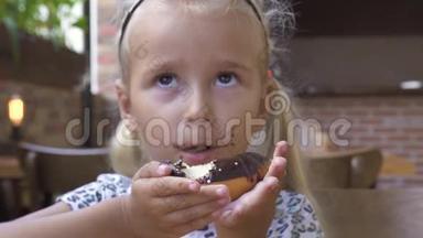 肖像小女孩在咖啡馆的桌子上吃甜巧克力甜甜圈。 可爱的金发女孩咬着巧克力甜甜圈