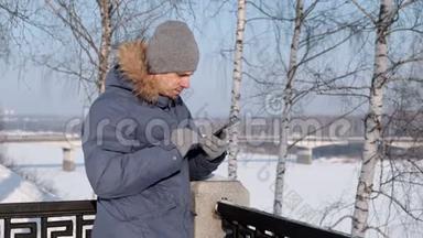 穿着带皮帽的蓝色羽绒服的人在冬季公园用手机摘下一只手套。