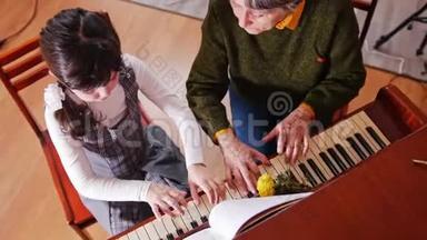 <strong>音乐</strong>课。弹钢琴的女孩，年长的<strong>老师</strong>坐在旁边和女孩一起弹。俯视图