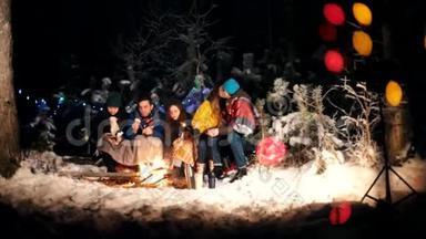 冬天森林里坐在火堆旁的年轻人。可<strong>爱</strong>的情侣<strong>之吻</strong>。快乐的朋友们