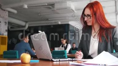 一个姜黄色的女人坐在办公室，用笔记本电脑做笔记