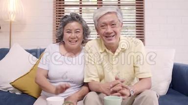亚洲老年夫妇在家客厅里躺在沙发上与孙子一起使用智能手机视频会议。