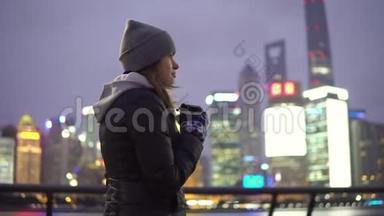 一个穿着黑色夹克和帽子的年轻女孩手里拿着咖啡在美丽的上海走来走去
