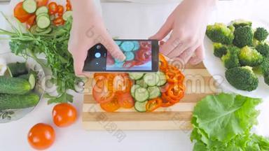 女人`手拿着智能手机，正在为沙拉拍摄新鲜蔬菜的<strong>照片</strong>，<strong>切</strong>片在<strong>切</strong>割板上。