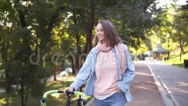 快乐的，微笑的女孩在早晨公园里除了一辆自行<strong>车外</strong>还散步。 那个女人骑着她的自行<strong>车</strong>走路，手里拿着