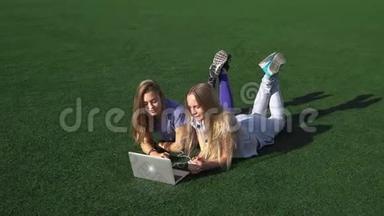 两个女孩用笔记本电脑躺在草地上。 高清高清