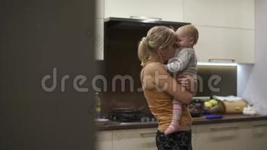 妈妈把一岁的女儿抱在怀里，抱着她的拥抱.. 厨房，人工照明，孩子很高兴