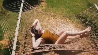 一位身穿泳装的年轻美女躺在吊床上，围着热带植物休息