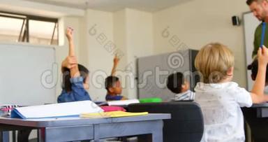 多民族学龄儿童在学校4k教室里坐在课桌前举手