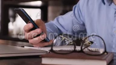 盖伊的特写`手里拿着一个电话。 桌子上有一个笔记本电脑眼镜和一个笔记本。