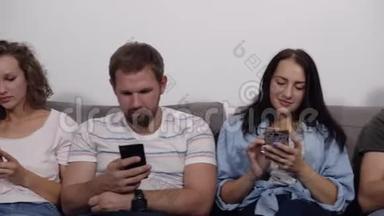 不同的年轻人排成一排坐在灰色的沙发上，痴迷于在线设备，白种人<strong>沉迷</strong>于使用