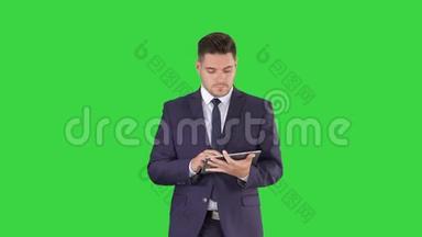 <strong>穿西装的人</strong>走路，在绿色屏幕上使用数字平板电脑，Chroma键。