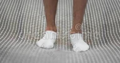 白色袜子的脚特写在蹦床网格上，摆动以缓慢的运动跳跃。 演讲的开始。