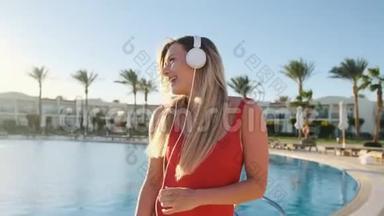 美丽的女士穿着红色泳衣和耳机，在清澈的蓝色游泳池背景下跳舞，玩得<strong>开心</strong>，听得<strong>开心</strong>