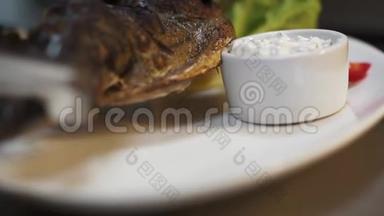 厨师把煮熟的鲭鱼鱼放在大盘子里，用金属钳子把白酱、柠檬、胡椒和生菜放在盘子里