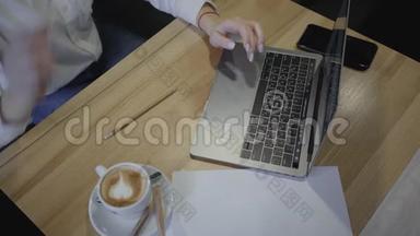 在咖啡馆或餐馆里使用笔记本电脑的女人的俯视图。 头顶射中坐在桌子旁端着杯子的年轻女子